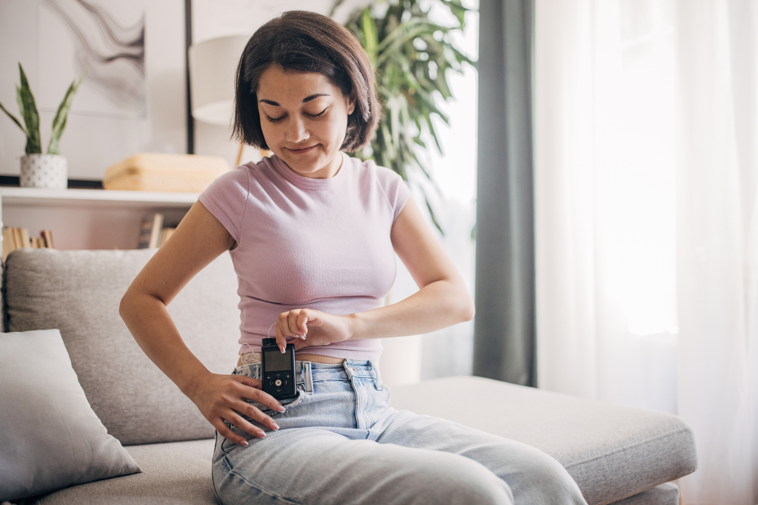 Woman attaching a device to her belt on the sofa.
