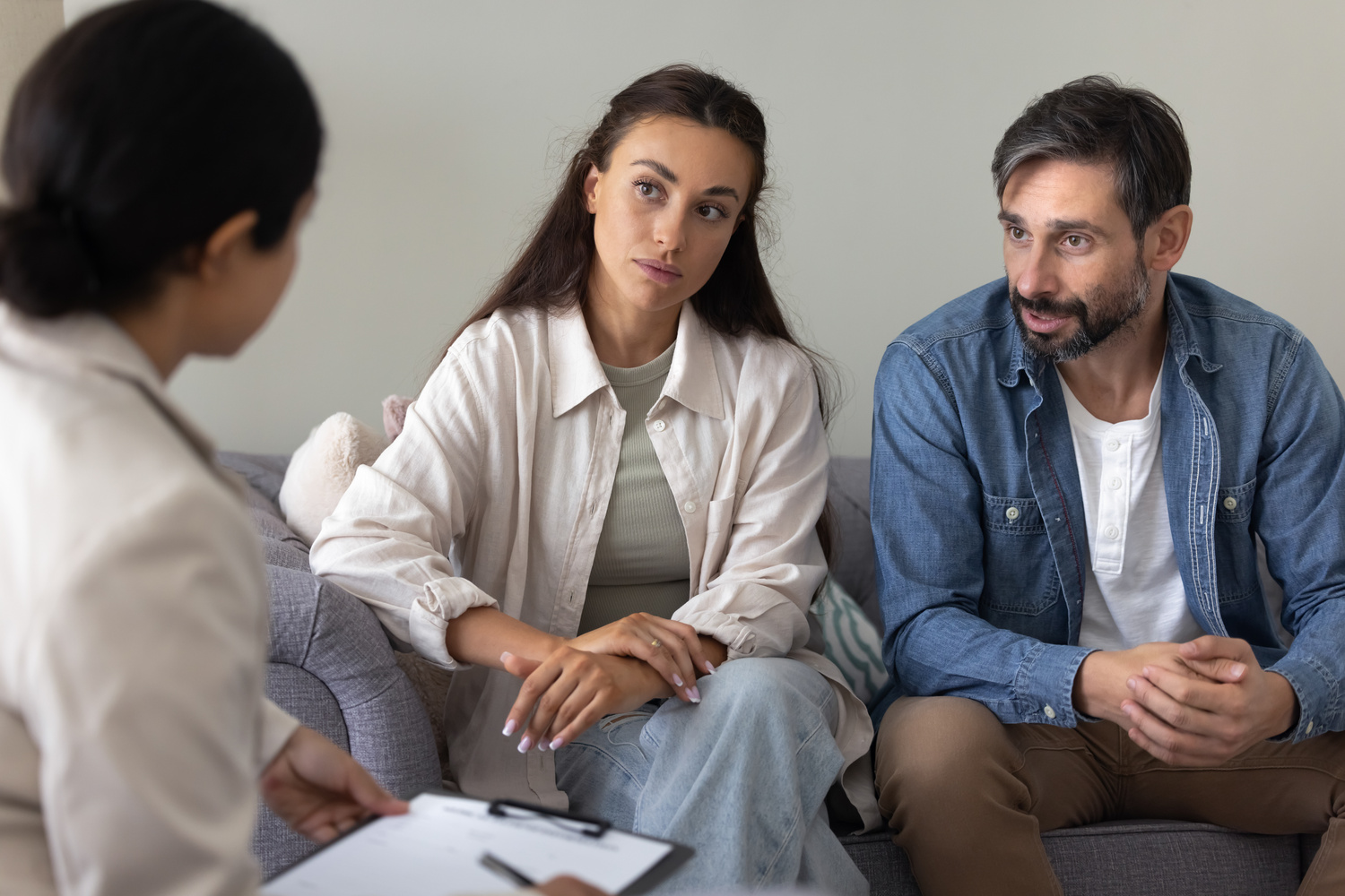 Serious married couple sitting on sofa talking to female psychologist